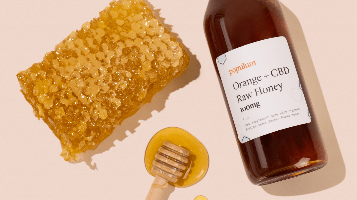 Populum Orange + CBD Honey posed with a honeycomb and a wooden honey dipper that's dripping with honey.